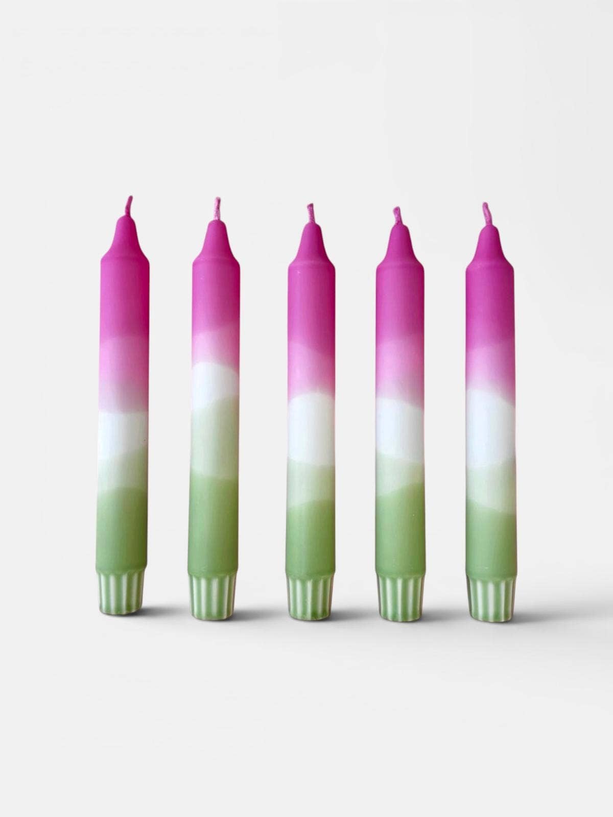 Five taper candles with a vertical ombré color design of pink, white, and light green, standing upright against a plain light gray background.