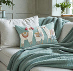 Decorative pillow with llama design on a couch with a green blanket