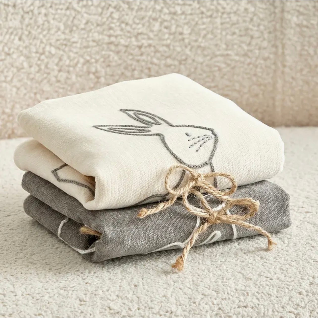 Stack of folded cushion covers with embroidered bunny design on a textured surface