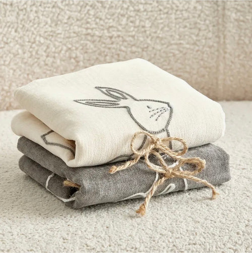 Stack of folded cushion covers with embroidered bunny design on a textured surface