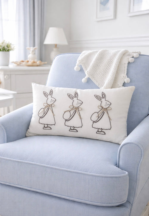 Decorative pillow with rabbit illustrations on a light blue armchair in a bright room.