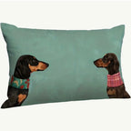 Decorative pillow with two dachshunds wearing colorful sweaters on a teal background
