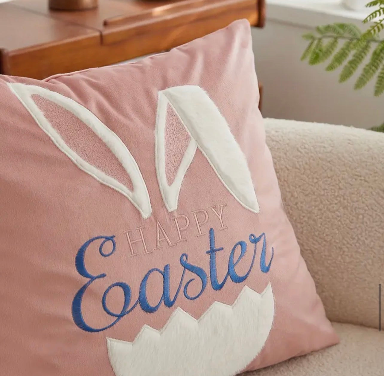Pink pillow with 'Happy Easter' text and bunny ears on a couch.