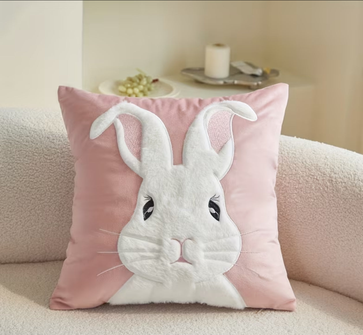 Pink pillow with a white rabbit design on a beige couch.