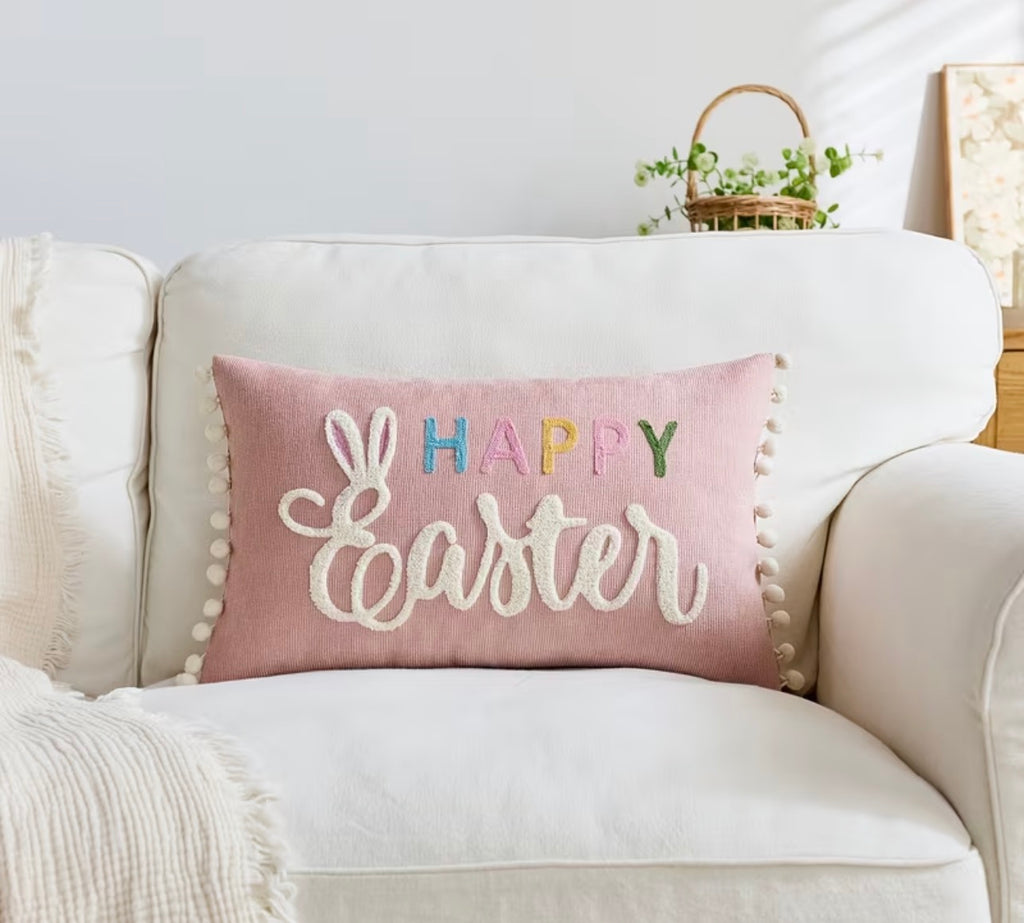 Pink 'Happy Easter' pillow on a white couch with a decorative basket in the background.