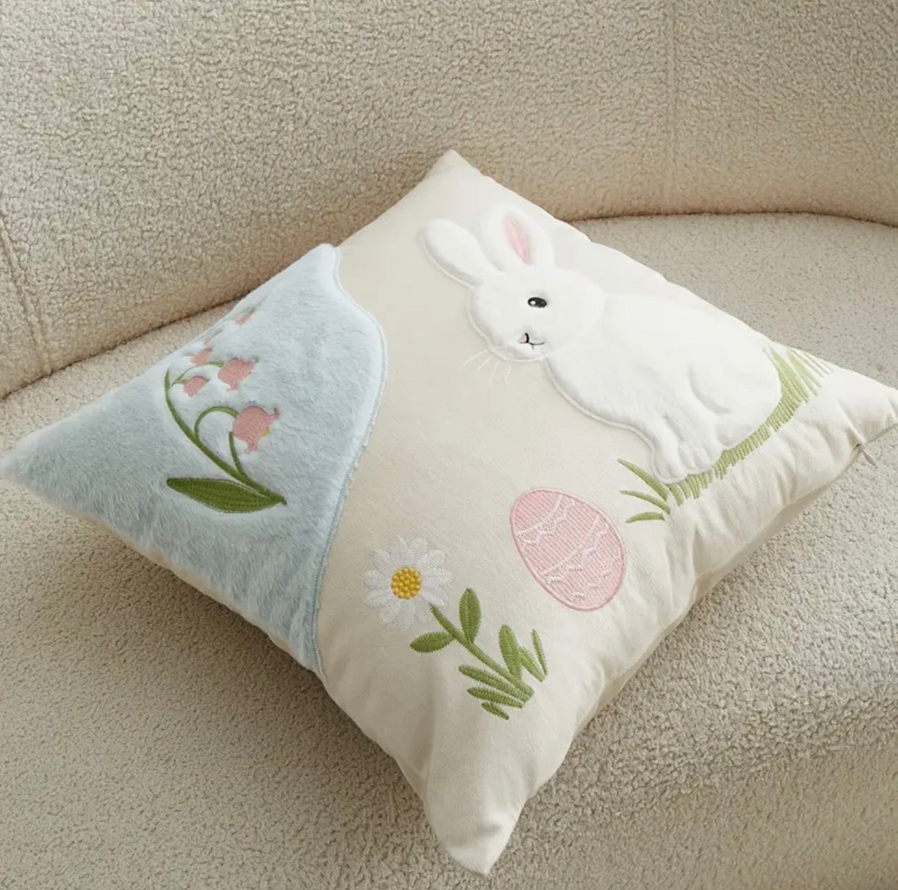 Decorative pillow with bunny and floral designs on a beige couch.