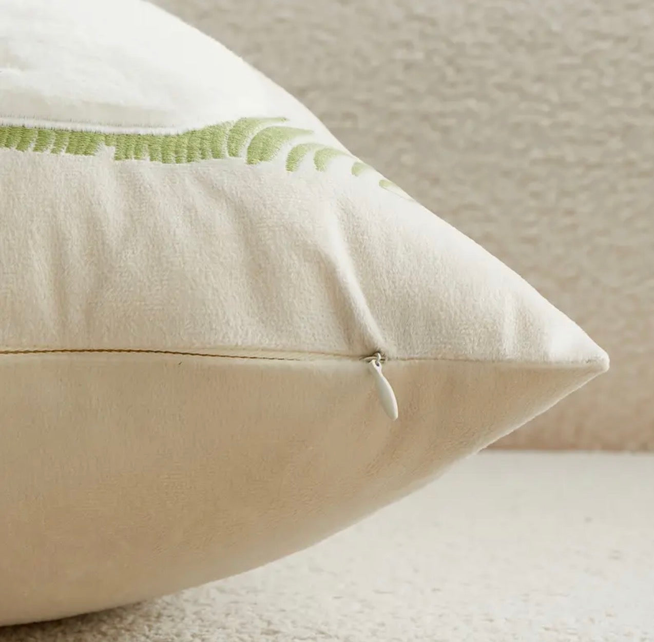 Beige pillow with green embroidery on a neutral background