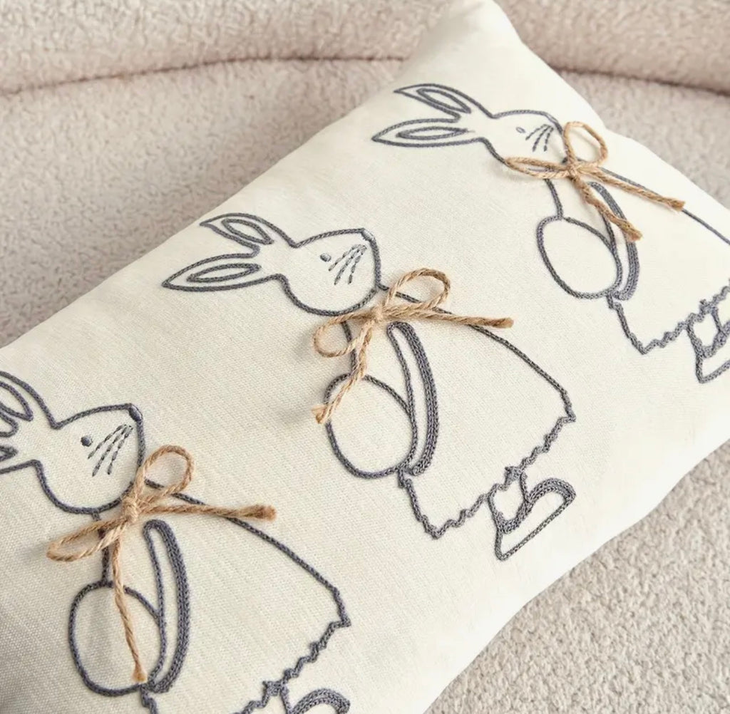 Decorative pillow with embroidered bunny and egg patterns on a neutral background