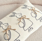 Decorative pillow with embroidered bunny and egg patterns on a neutral background