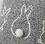 Gray textured pillow with white embroidered design and pom-pom detail