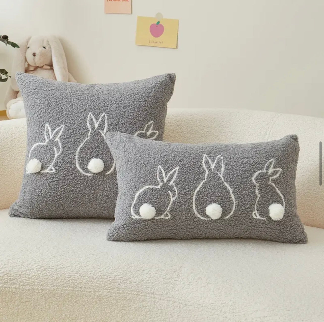 Two gray pillows with bunny designs on a beige couch.