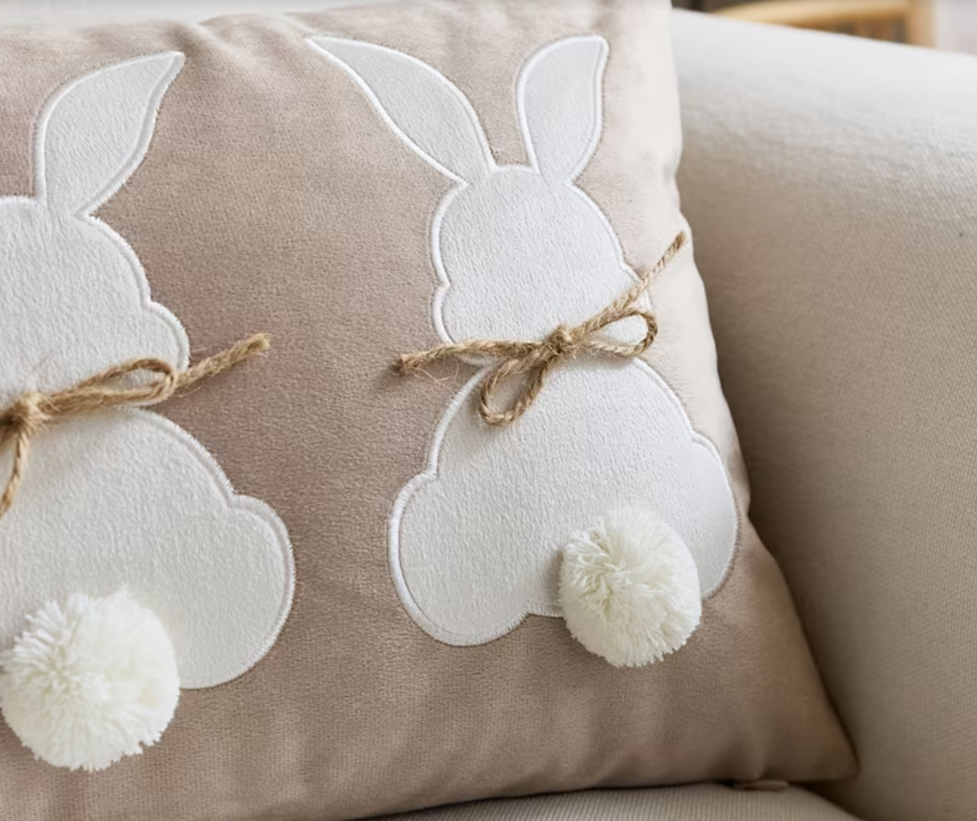 Decorative pillow with white bunny shapes and pom-poms on a beige background