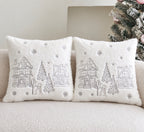 Two square white faux-fur throw pillows with embroidered winter village scenes, displayed on a beige sofa next to a decorated Christmas tree.