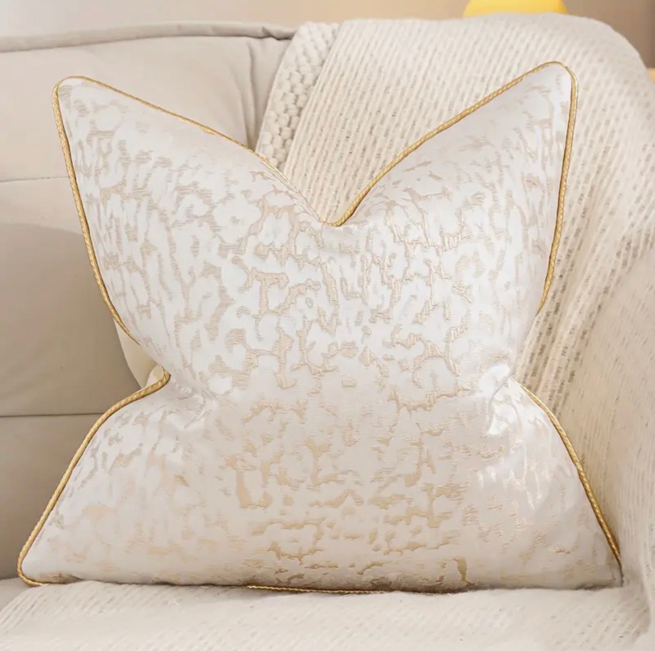 Decorative pillow with textured pattern and gold trim on a beige sofa.