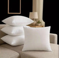 White pillows on a beige sofa with a lamp and plant in the background