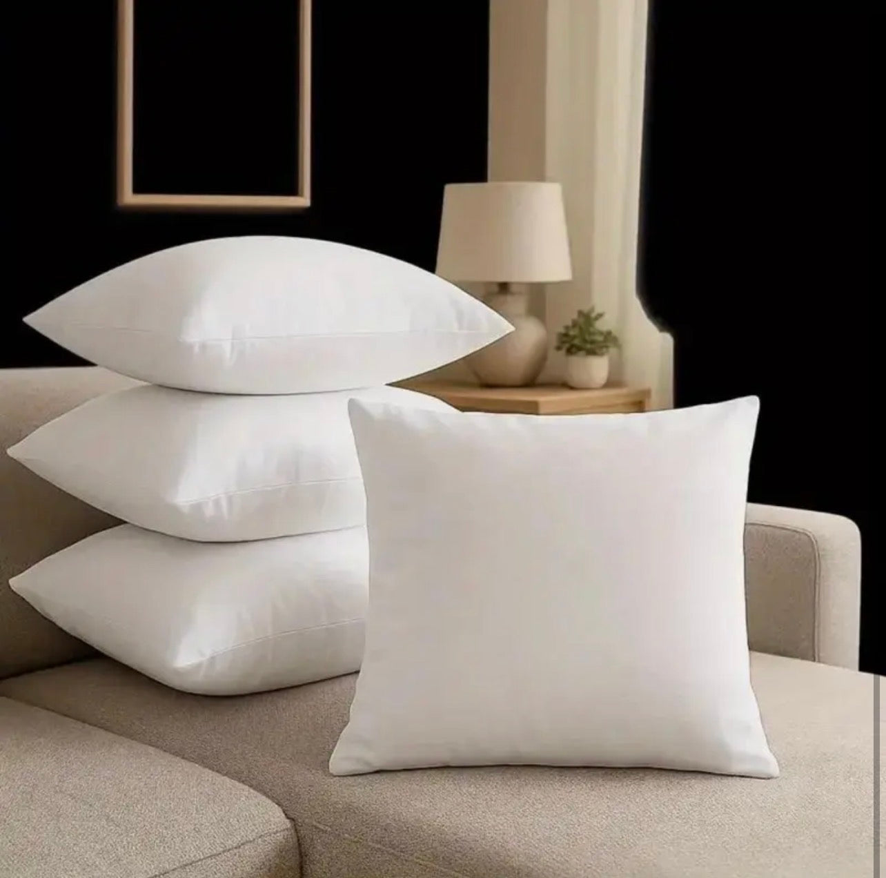 White pillows on a beige sofa with a lamp and plant in the background