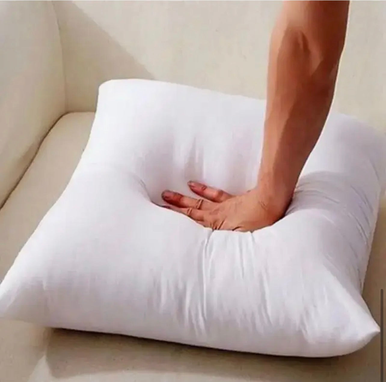 Person holding a white pillow on a beige couch