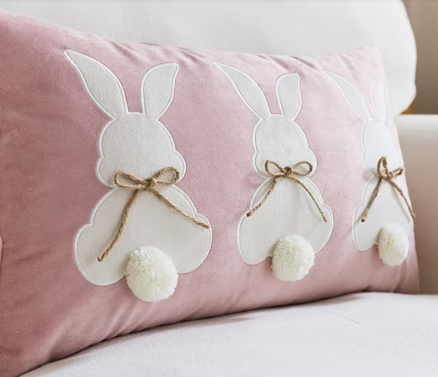 Pink pillow with white bunny designs and pom-poms on a light background