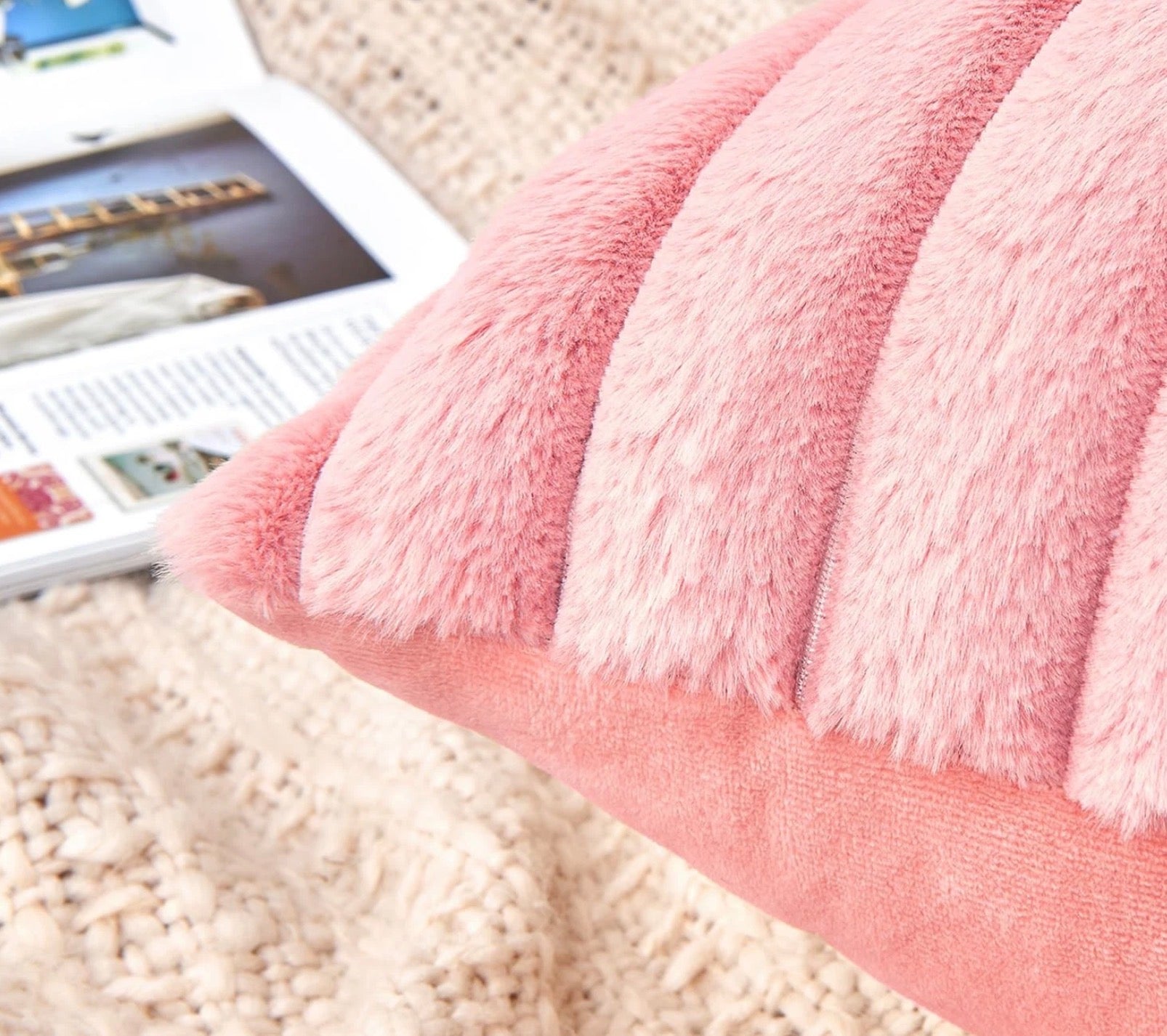 Close-up of a fluffy pink pillow on a textured surface with a magazine in the background.