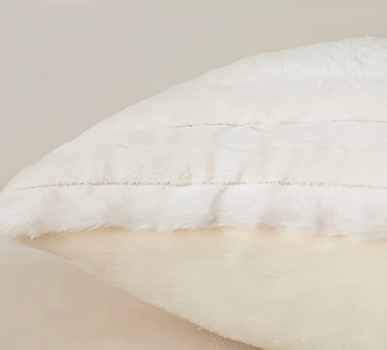 Close-up of a white quilted pillow with beige interior on a neutral background