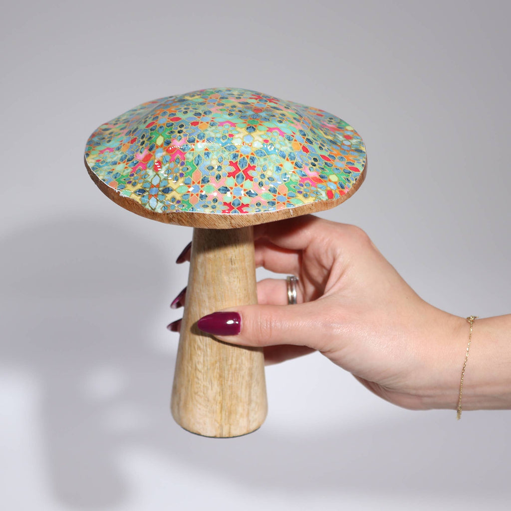 Hand holding a wooden mushroom with a colorful, speckled cap against a gray background