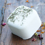 White bath bomb with green herbs on a wooden surface with dried flowers