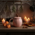 Pink pumpkin-shaped mug with a lid on a white surface with autumn leaves.