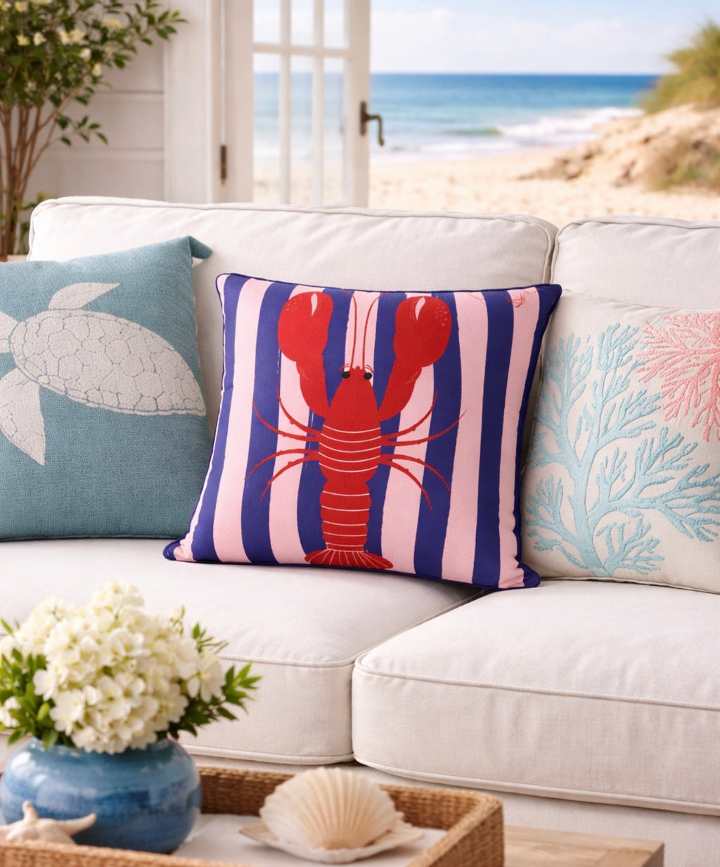Decorative pillows with a lobster design on a white couch by a window with a view of the ocean.