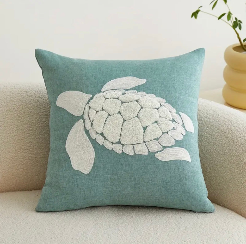 Teal pillow with a white turtle design on a beige couch.
