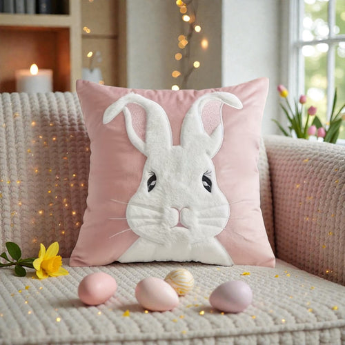 Decorative pillow with a bunny design on a couch with Easter eggs and flowers.